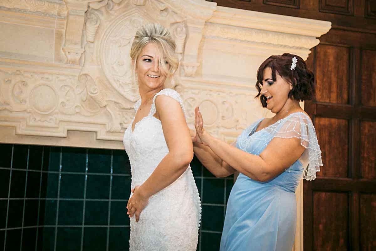 bridesmaid doing up brides dress