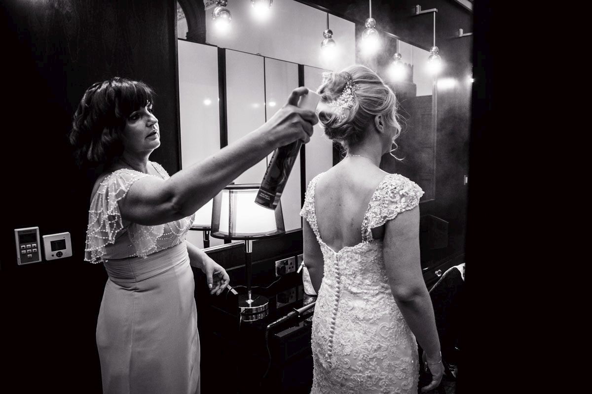 bridesmaid spraying hairspray on the brides hair