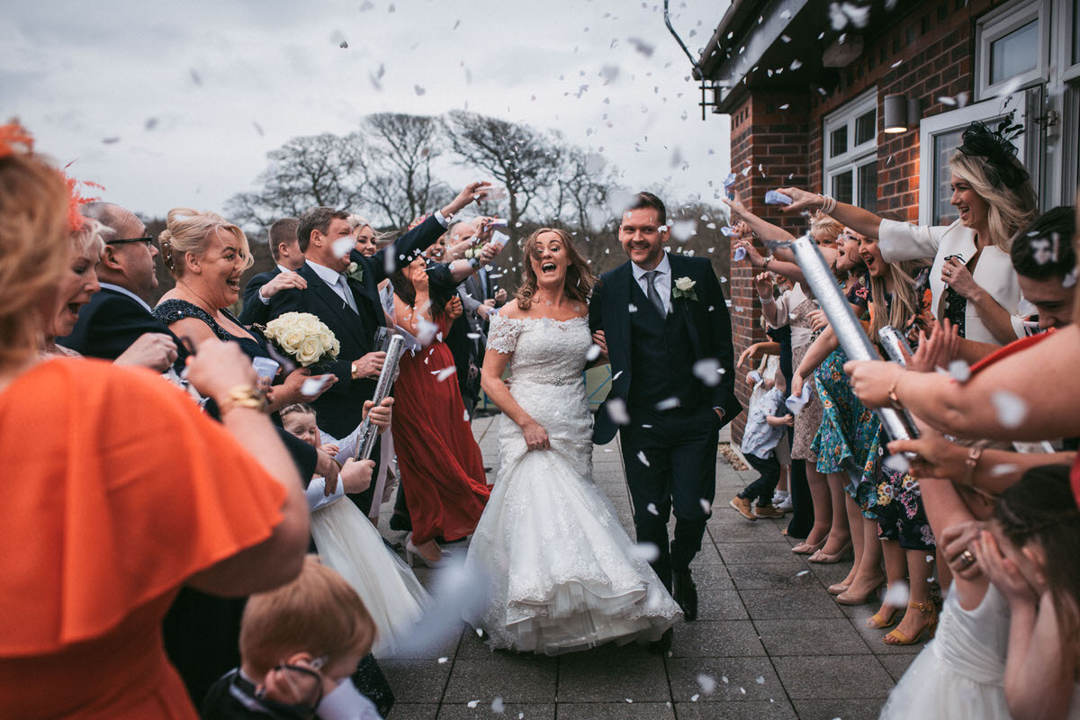 guests throw confetti at the couple on their wedding day at formby hall by liverpool wedding photographer
