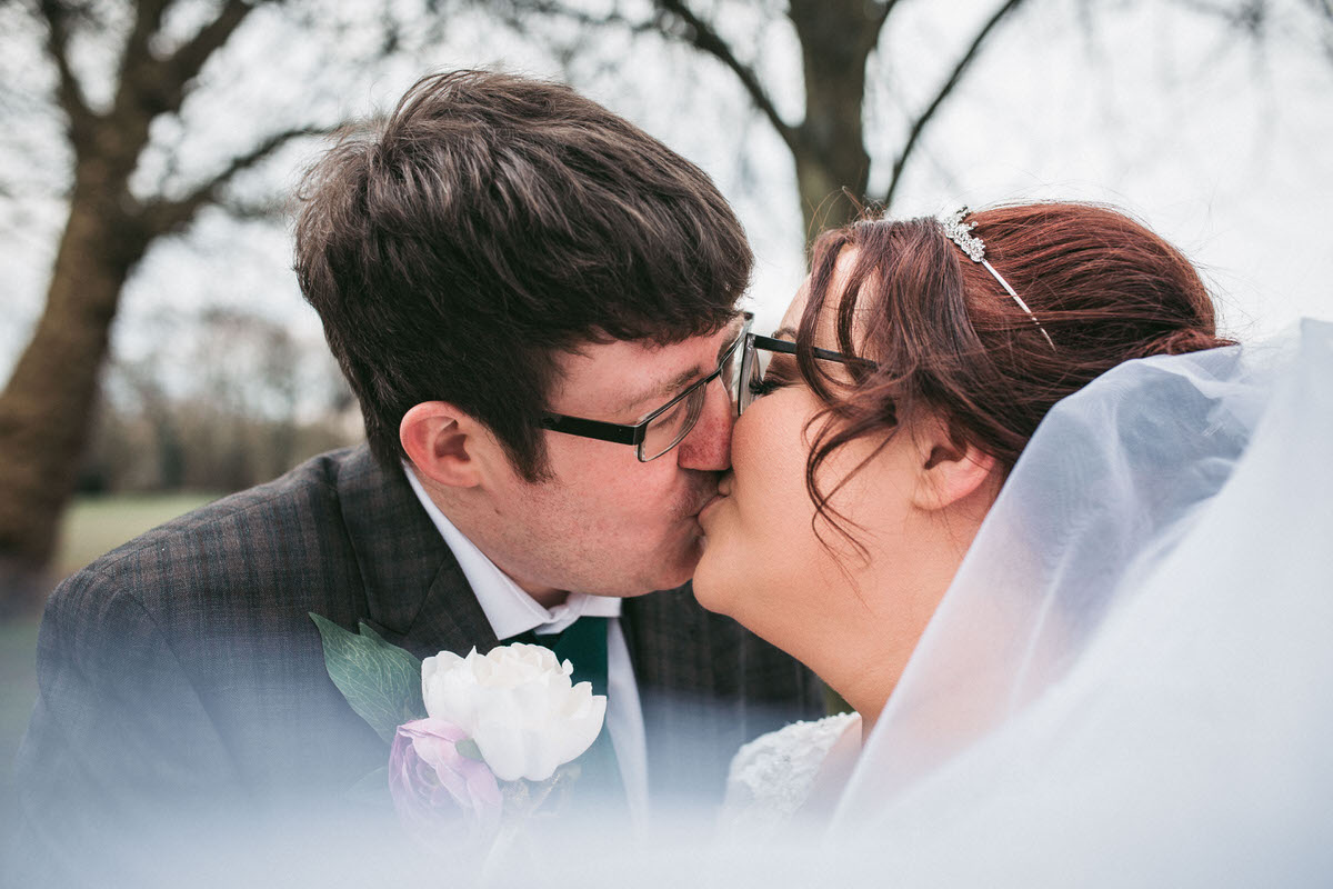 Veil blows in the wind as bride and groom kiss in sefton park liverpool