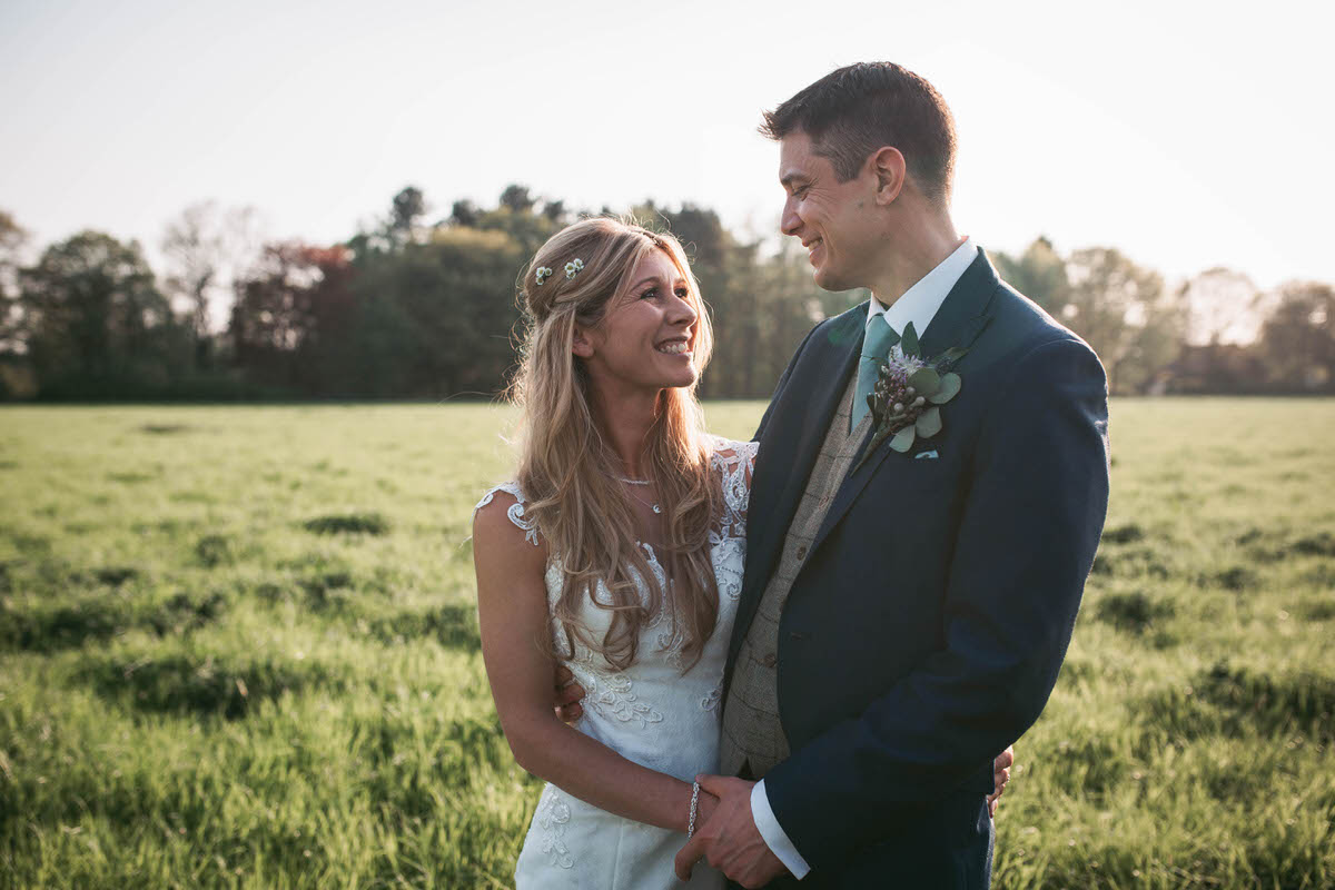 bride and groom smile at each other in a field at owen house wedding barn