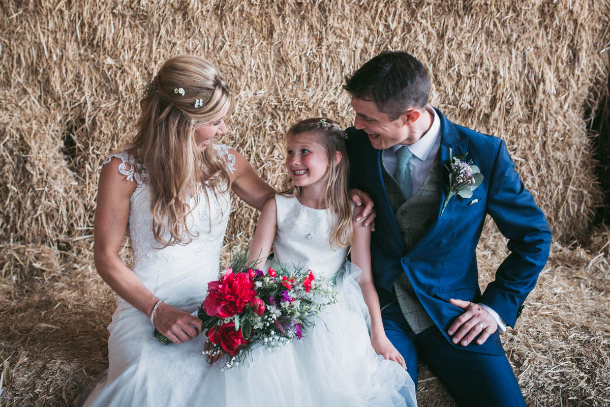 bride and groom with their daughter on the hay bales at owen house wedding barn