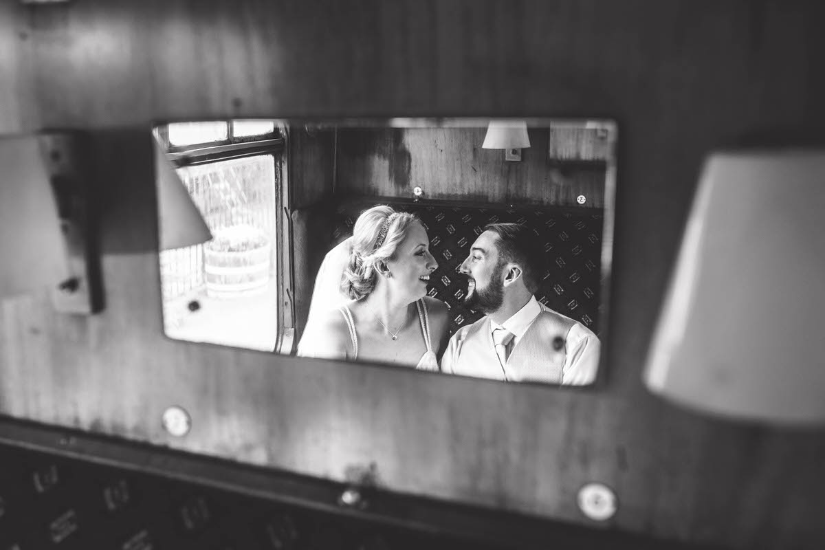 on a carriage on a train at llangollen railway station photo of bride and groom in the reflection of a mirror in black and white