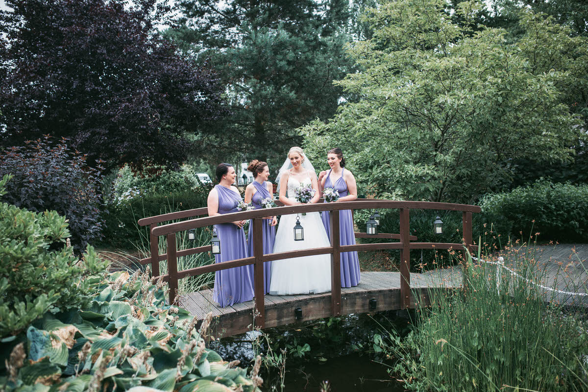bride and bridesmaids laughing on a bride over a pond at wild pheasant hotel llangollen