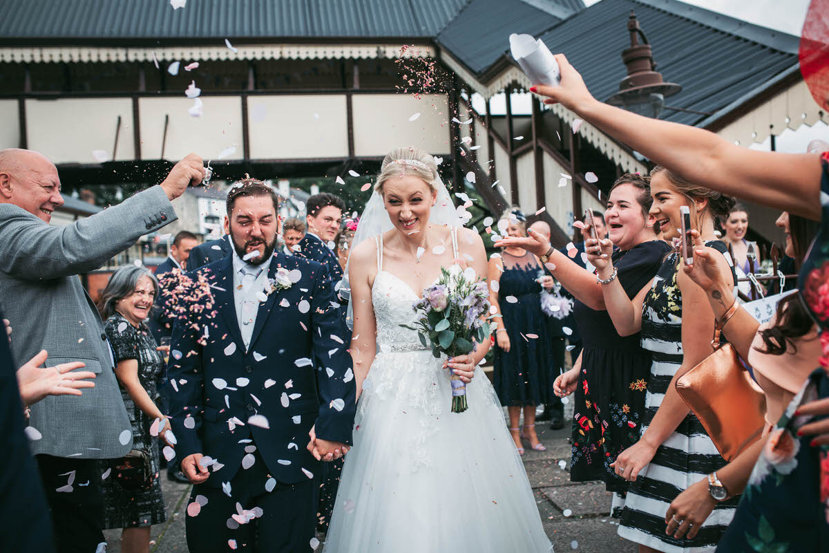 bride and groom rung through the confetti thrown by guests on the platform at llangollen railway station